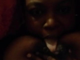 Busty Ebony sucking both her nipples in bed